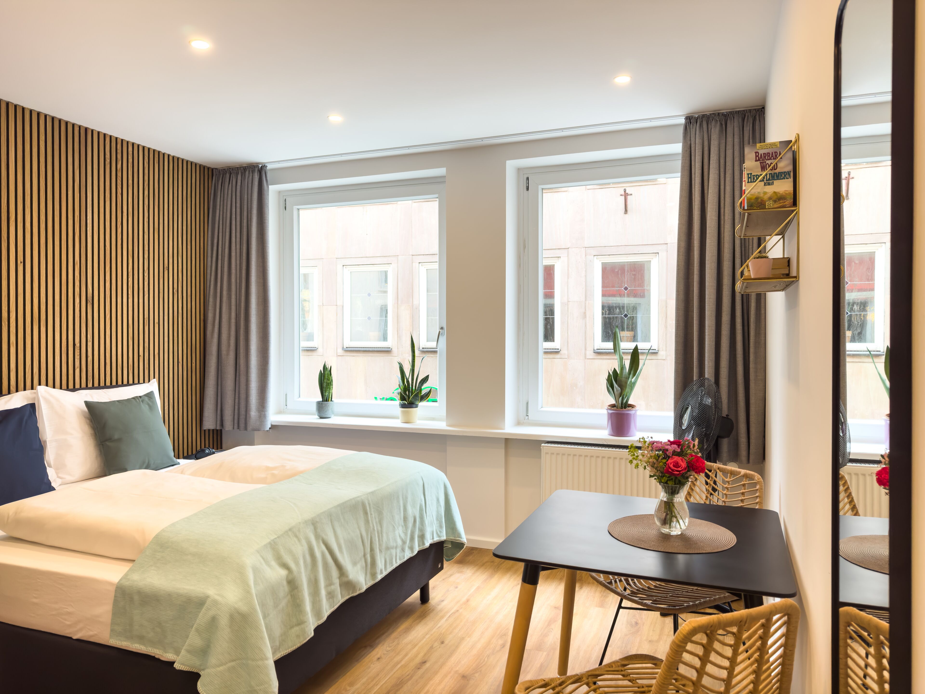 A hotel room with a bed, a small table with chairs, a window with curtains, and a radiator.