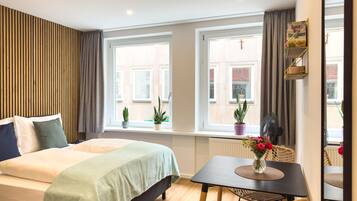 A hotel room with a bed, a small table with chairs, a window with curtains, and a radiator.