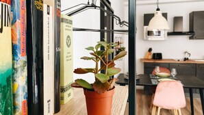 A bookshelf with books, a potted plant, and a kitchen area in the background.