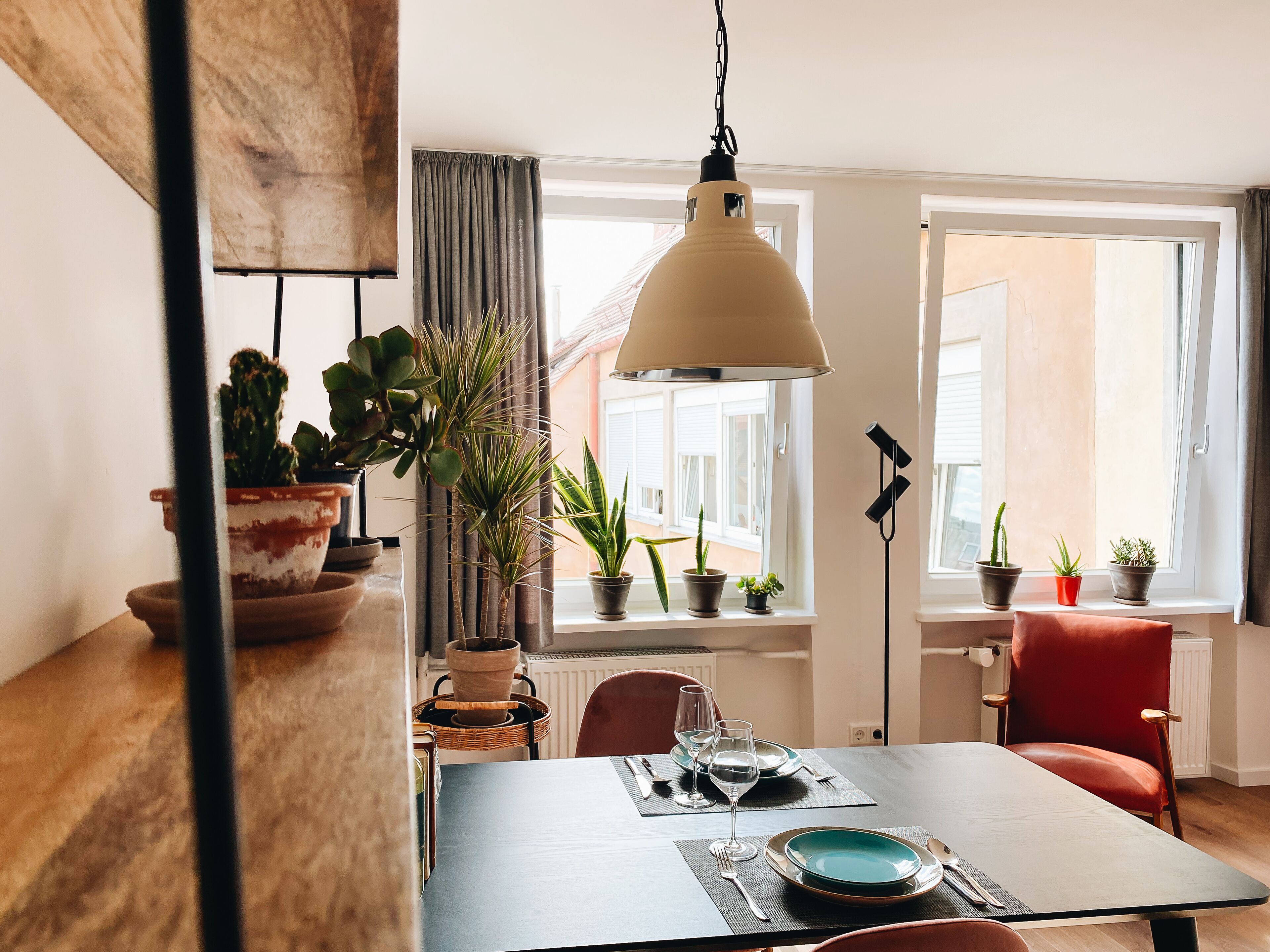 A dining area with a table set for two, potted plants, and a red chair.