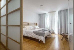 A bedroom with a wooden bed, white bedding, and a view of the outdoors through large windows. - Market Place F 2BR duplex (historical city center) (Ponta Delgada)