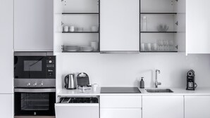 Una cocina moderna con armarios blancos, horno empotrado, cafetera y fregadero.