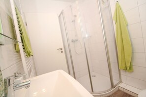 Une salle de bain avec une douche à parois de verre, un lavabo blanc et des serviettes vertes.