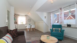 Un salon chaleureux avec un canapé, un fauteuil turquoise, une petite table en bois et un tapis à motifs.