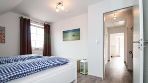 Une chambre moderne avec un lit, un bureau, un tableau et un couloir menant à une autre pièce.
