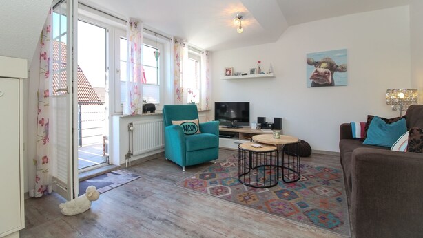 Un salon avec un fauteuil turquoise, un canapé marron, un téléviseur et un tapis à motifs.