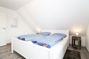 A white bed in a room with a sloped ceiling, two bedside tables with lamps, and a small mirror on the wall.
