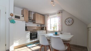 Une cuisine moderne avec des meubles blancs, un four encastré et un coin repas comprenant une table et des chaises.