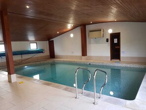 En inomhuspool med klart vatten, synliga träbjälkar i taket och ett kaklat golv.