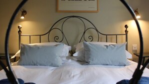 A bed with a metal frame, white bedding, and striped pillows. A framed sign with the word "PEACE" hangs on the wall above the bed.