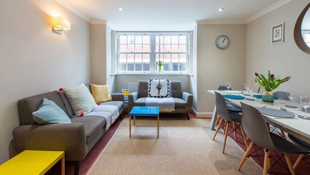 A modern living room with a sofa, coffee table, and dining area with chairs and a table set for two.