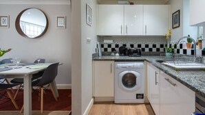 A compact kitchen with a washing machine, white cabinets, a checkered backsplash, and a dining area with a table and chairs.