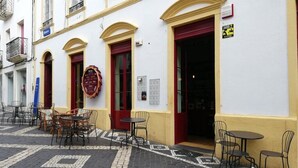 Un café situé au bord de la rue, avec des tables à l’extérieur, une porte rouge et une façade jaune et blanche.