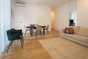 Un salon moderne avec un plancher en bois, un canapé beige, une table à manger avec des chaises et un fauteuil vert.