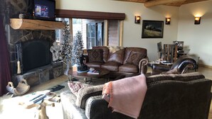 A cozy living room with a stone fireplace, leather sofas, a television, and a Christmas tree. - Elk Run Ranch…Come enjoy the breath taking views of Paradise Valley & YNP (Emigrant)