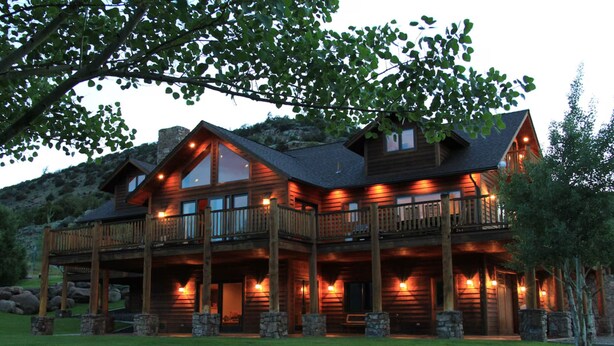 A large, multi-story log cabin with a balcony, stone pillars, and a well-lit exterior. - Elk Run Ranch…Come enjoy the breath taking views of Paradise Valley & YNP (Emigrant)