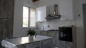 A modern kitchen with white cabinetry, a stainless steel range hood, and a dining table with chairs.