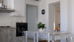 A modern kitchen with white cabinetry, a gas stove, and a built-in oven. There is a dining table with chairs and a potted plant.