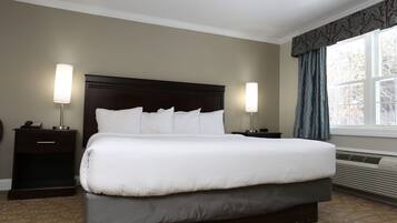 A hotel room with a large bed, two bedside tables with lamps, a window with curtains, and a wall-mounted heater.