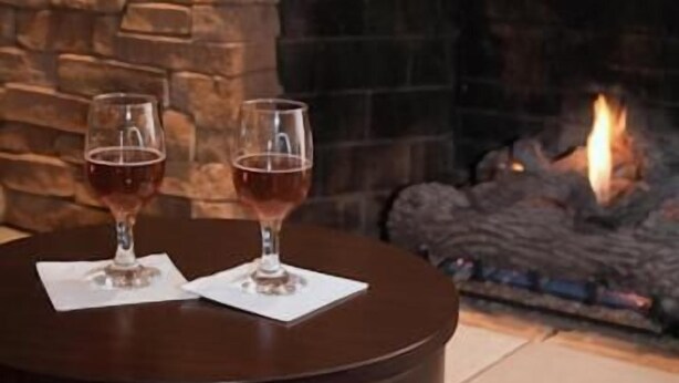 A stone fireplace with two glasses of red wine on a round table. - Golden Apple Inn (Glen)
