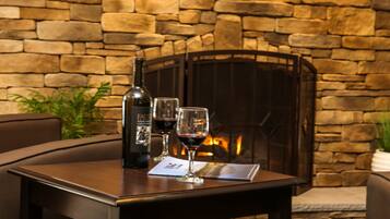 A table with a bottle of wine, two glasses, and a menu in front of a stone fireplace.