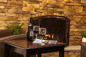 A table with a bottle of wine, two glasses, and a menu in front of a stone fireplace.