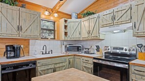 A kitchen with wooden cabinets, a microwave, a stove, and a dishwasher. - Log Cabin with Creekside Covered Porch & Outdor Hot Tub! (Bryson City)