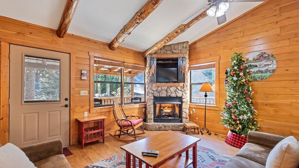 A cozy log cabin interior with a stone fireplace, wooden walls, a Christmas tree, and a comfortable seating area. - Log Cabin with Creekside Covered Porch & Outdor Hot Tub! (Bryson City)