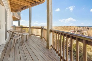 A wooden deck with a view of the beach, a covered seating area, and a wooden railing.