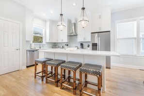 A modern kitchen with white cabinetry, a central island with bar stools, stainless steel appliances, and pendant lighting.