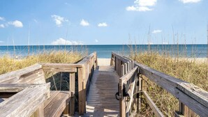 Una passerella di legno che conduce a una spiaggia, con cielo sereno e acque calme.