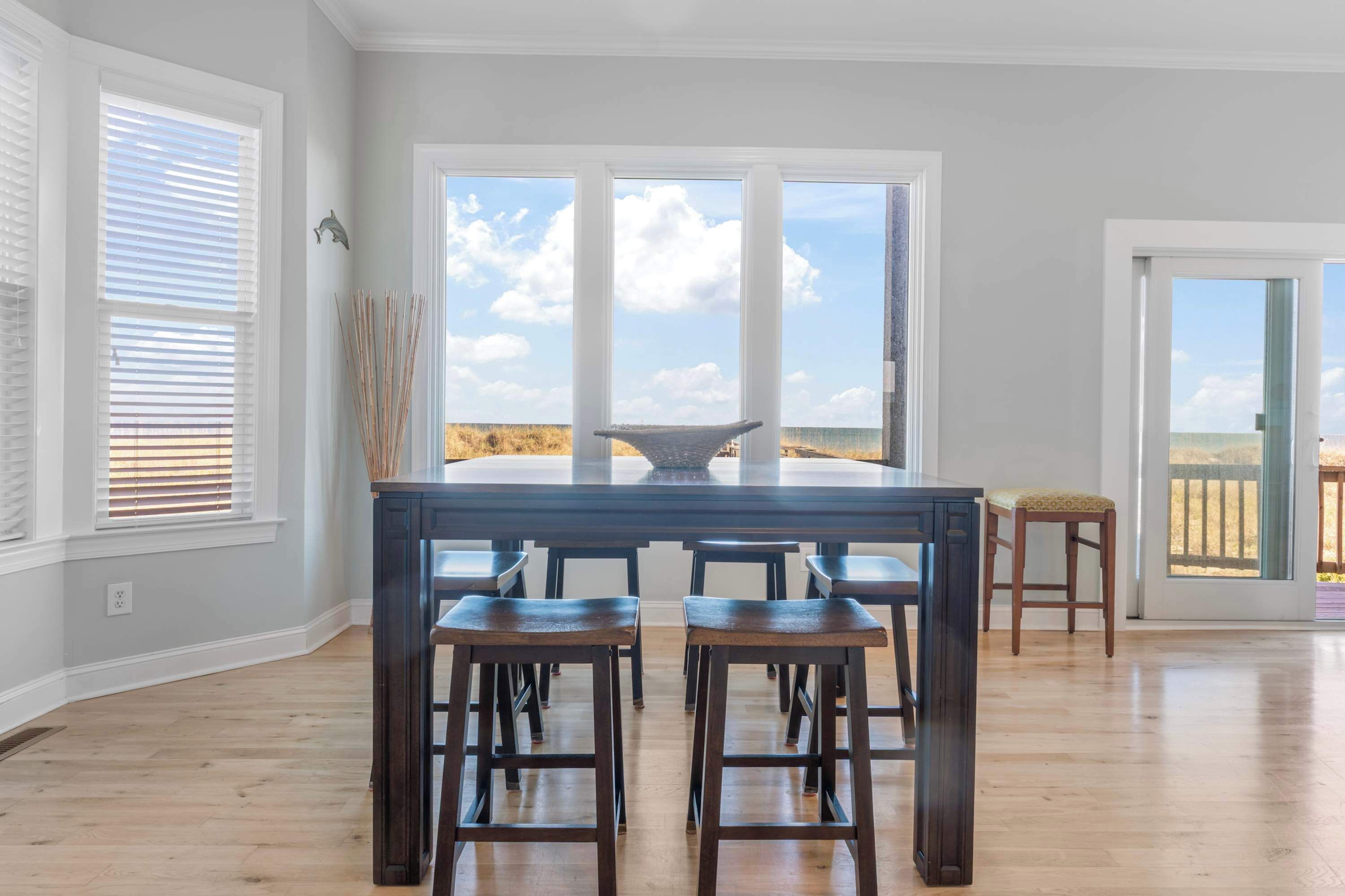 A spacious kitchen with a large island, multiple bar stools, and a view of the beach through large windows.