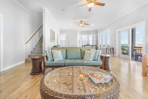 A spacious living room with a wooden floor, a round glass coffee table, a green sofa, and a ceiling fan.