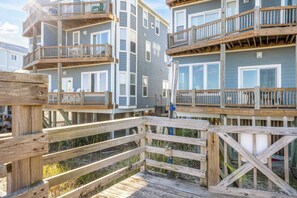 A multi-story wooden deck with balconies, overlooking a beach area.