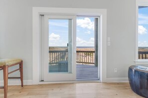 A room with a wooden floor, a sliding glass door leading to an outdoor deck, a wooden chair, and a round table.