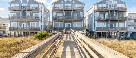 A beachfront property with a wooden boardwalk leading to a multi-story building with balconies.