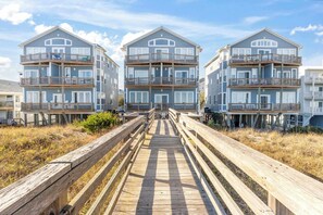 A beachfront property with a wooden boardwalk leading to a multi-story building with balconies.