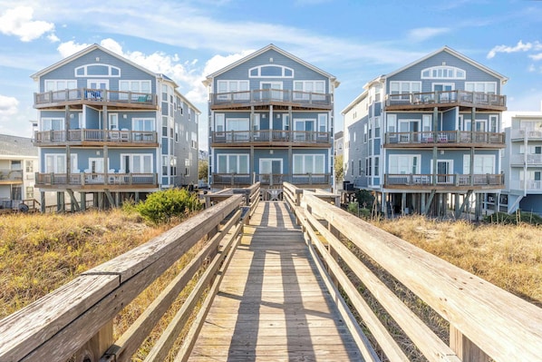 A beachfront property with a wooden boardwalk leading to a multi-story building with balconies.