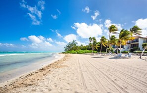 Une plage avec un ciel dégagé, des palmiers et un bâtiment doté d’un balcon.
