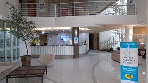 Un hall de hotel con mostrador de recepción, zona de estar, escalera y un cartel que promueve medidas de prevención contra el COVID-19.