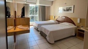 Una habitación de hotel con dos camas, un escritorio, un televisor y una ventana con cortinas.