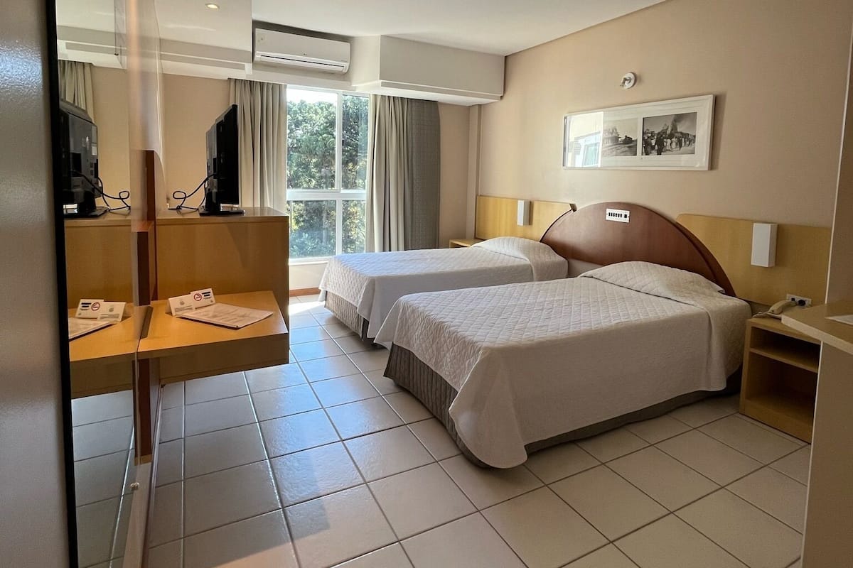 Une chambre d’hôtel avec deux lits, un bureau, une télévision et une fenêtre avec des rideaux.