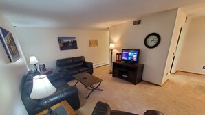 A living room with a sofa, coffee table, TV stand, and lamp. - Tomar Park Apt 3 - KP101APT3 (Sioux Falls)
