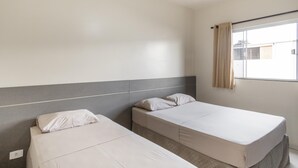 Una habitació d'hotel amb dos llits individuals, una finestra amb cortines i una paret senzilla.
