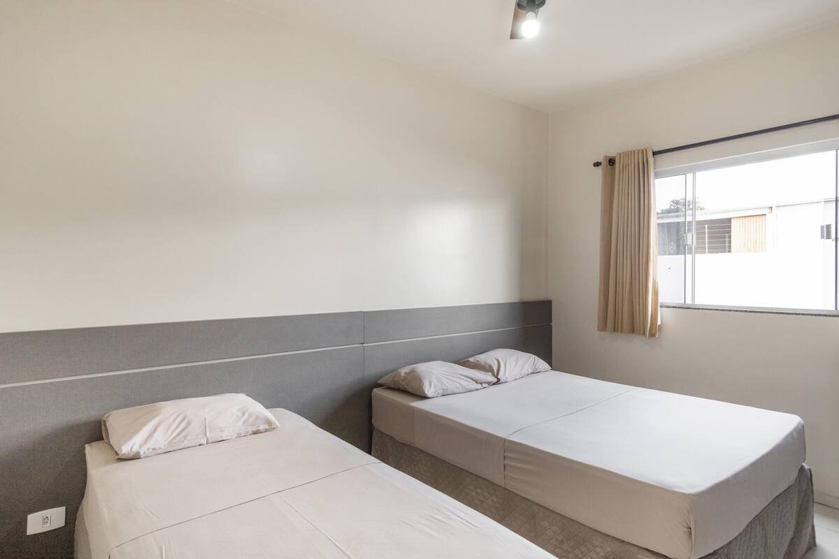 A hotel room with two single beds, a window with curtains, and a plain wall.