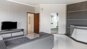 Un saló modern amb televisió de pantalla plana, un sofà gris i una porta de fusta que condueix a una altra habitació.