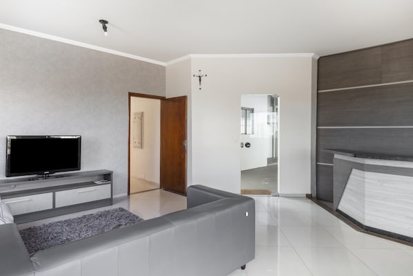 Un salón moderno con televisor de pantalla plana, sofá gris y puerta de madera que da a otra habitación.
