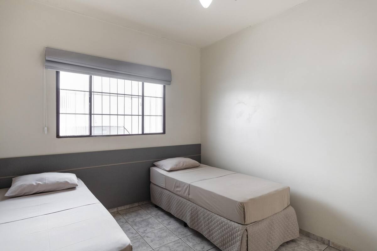 A small, clean room with a single bed, a window with blinds, and a plain wall.