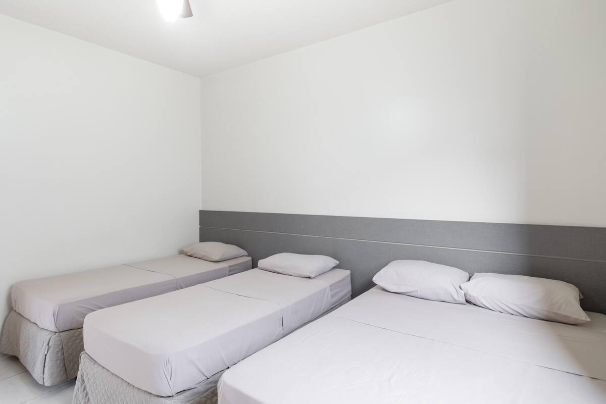 A hotel room with three single beds, each with a grey headboard and white bedding.