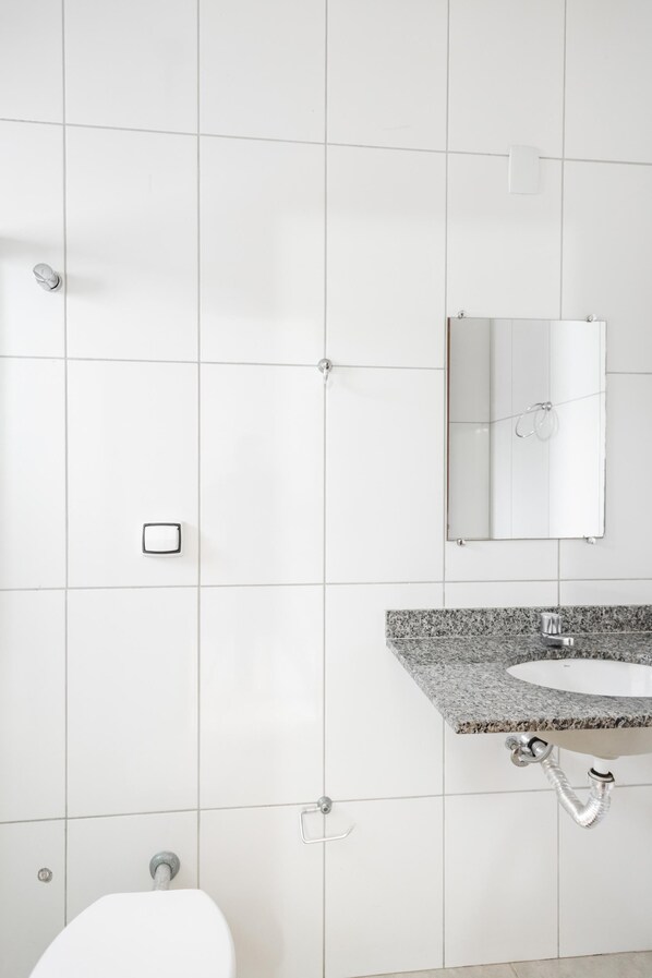 Un baño con paredes de azulejos blancos, un lavabo con encimera de granito, un espejo y un inodoro.